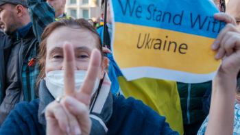 Eine Frau mit einer Ukraine-Flagge zeigt mit den Finger das Peace-Zeichen