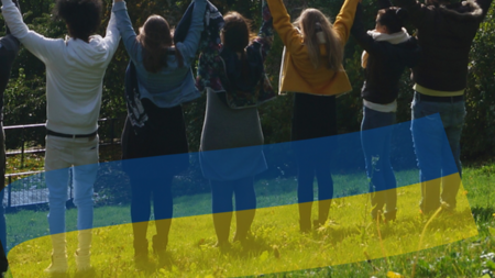 Junge Menschen in einer Reihe, die die Hände hochhalten, darüber die Ukraine-Flagge