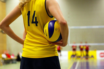 Rücken einer Volleyballspielerin in gelbem Trickot mit Volleyball unter ihrem Arm