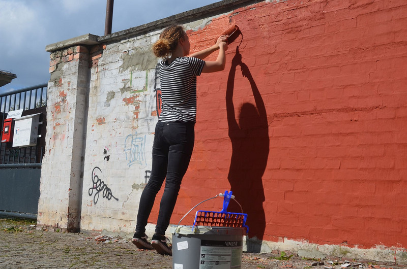 Eine Freiwillige streicht eine Fassade orange am Werk4
