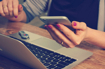 Person mit Handy in der Hand vor einem Laptop