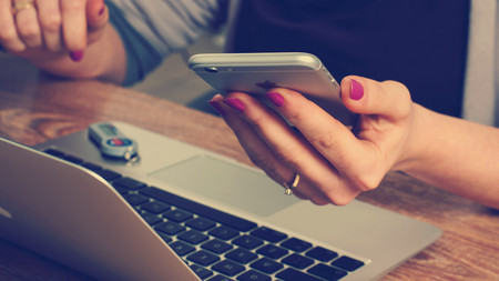 Person mit Handy in der Hand vor einem Laptop