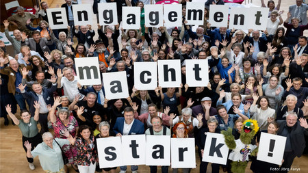 eine Menschengruppe hält Schilder mit den Worten "Engagement macht stark" nach oben