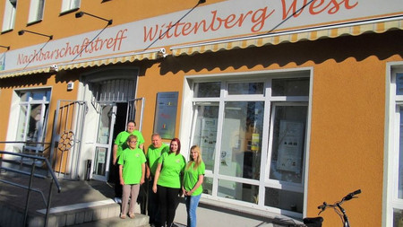 Fünf weiße Erwachsene in den gleichen neongrünen T-Shirts vor dem Eingang des Nachbarschaftstreffs Wittenberg West